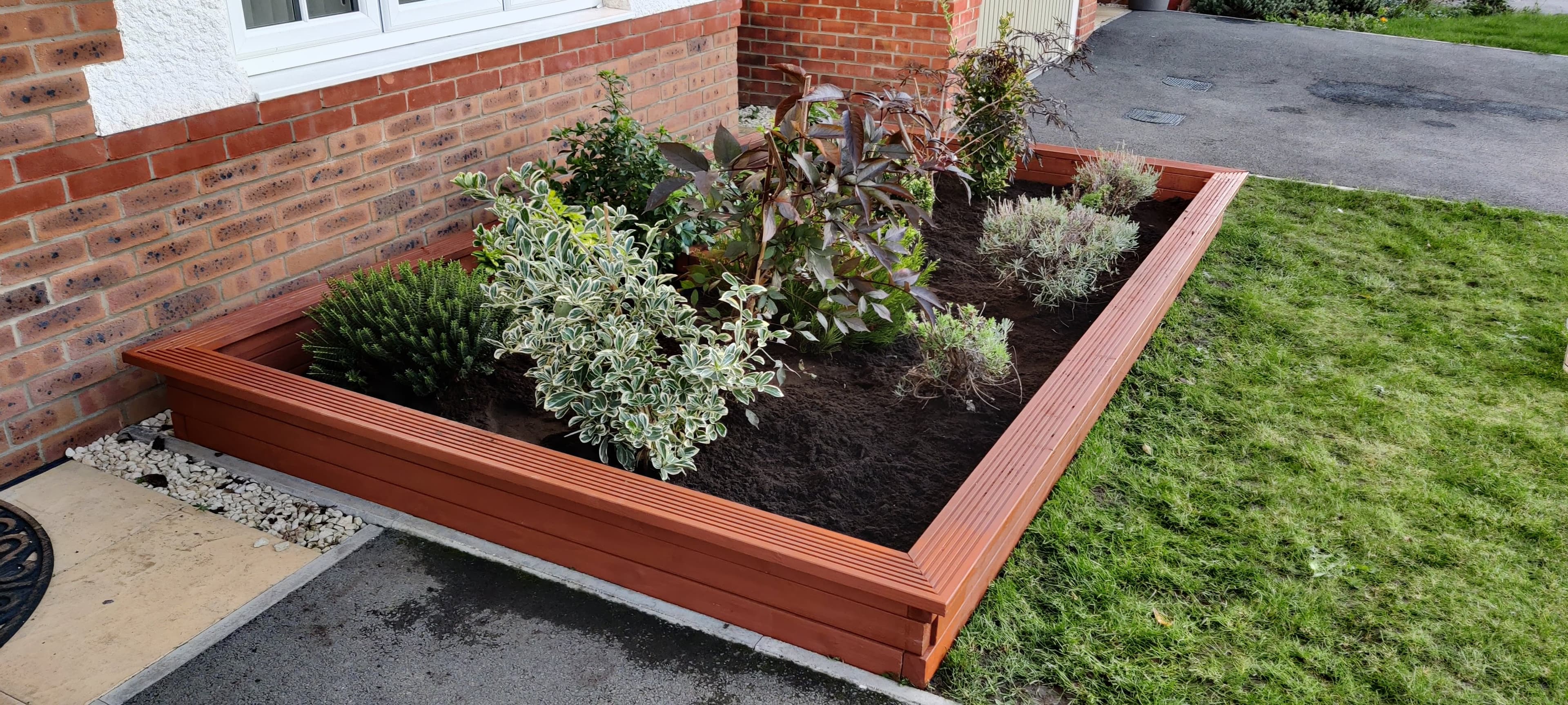 Finished redwood-stained raised corner planter bed with new shrubs planted